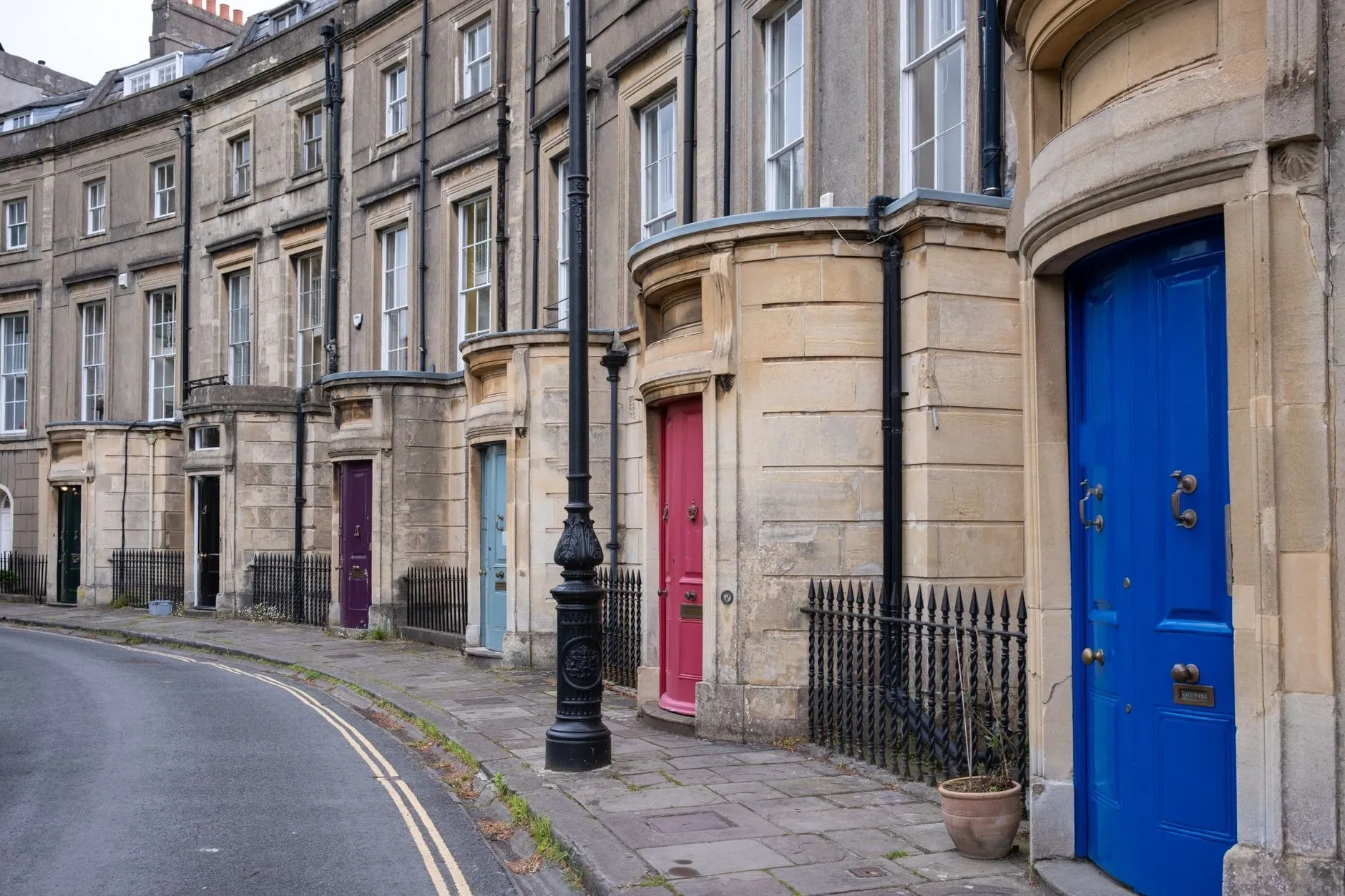 A curving Georgian terrace of Bath stone with painted front doors in blue, pink, purple and green