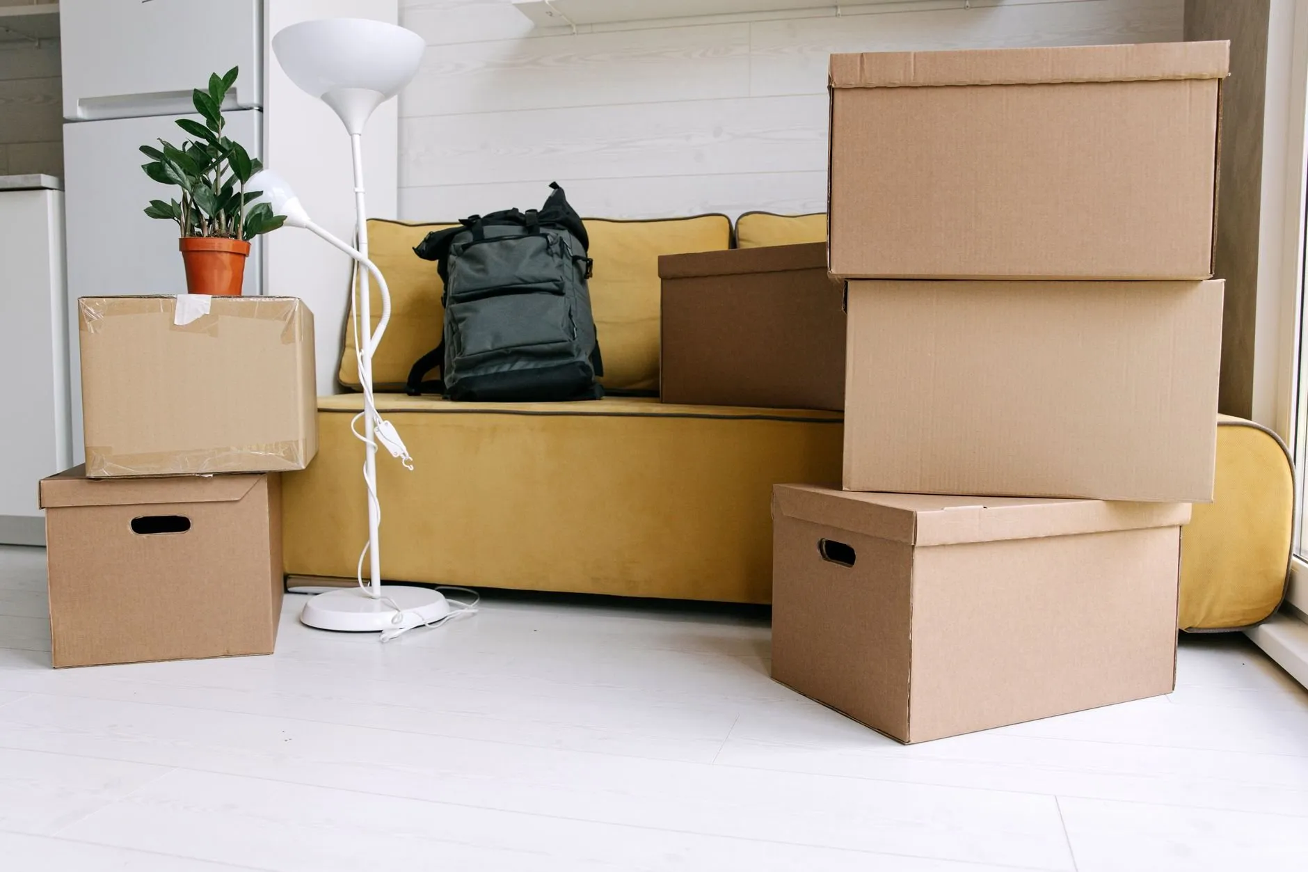 Moving boxes stacked beside a mustard sofa and a floor lamp