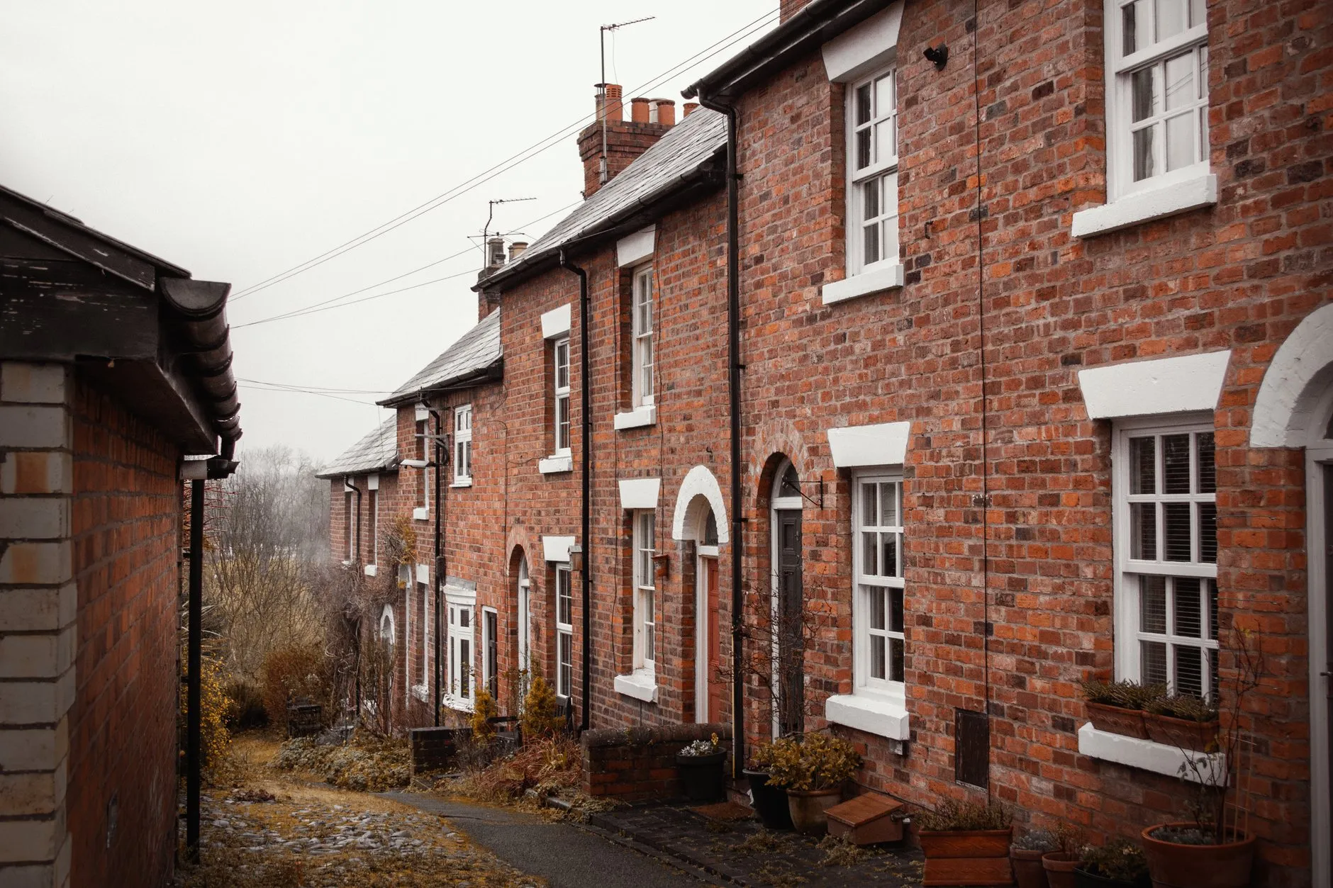 A row of red-brick terraced houses with white sash windows along a narrow lane