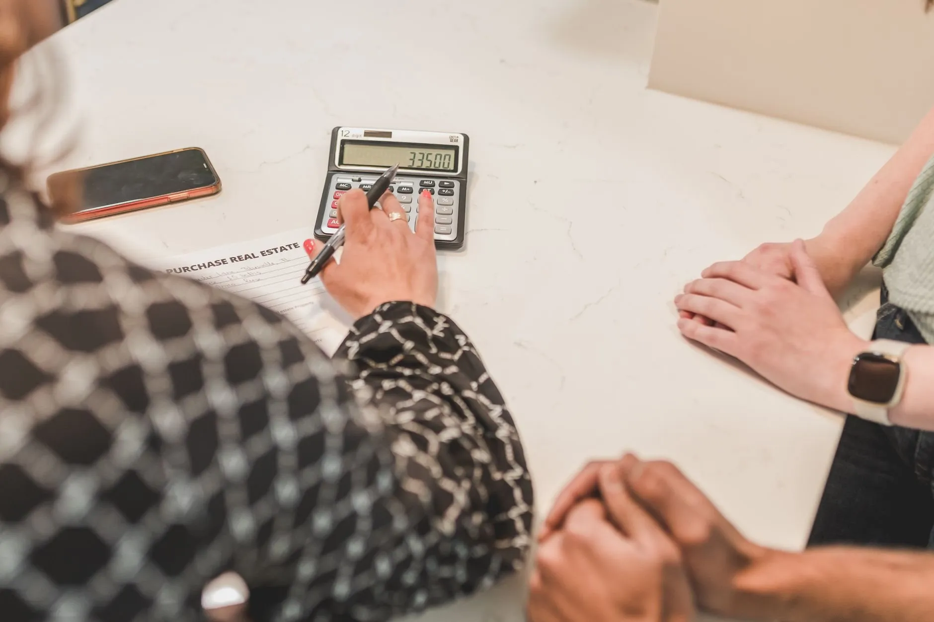 Two people's hands at a white table while an adviser works a calculator beside the paperwork