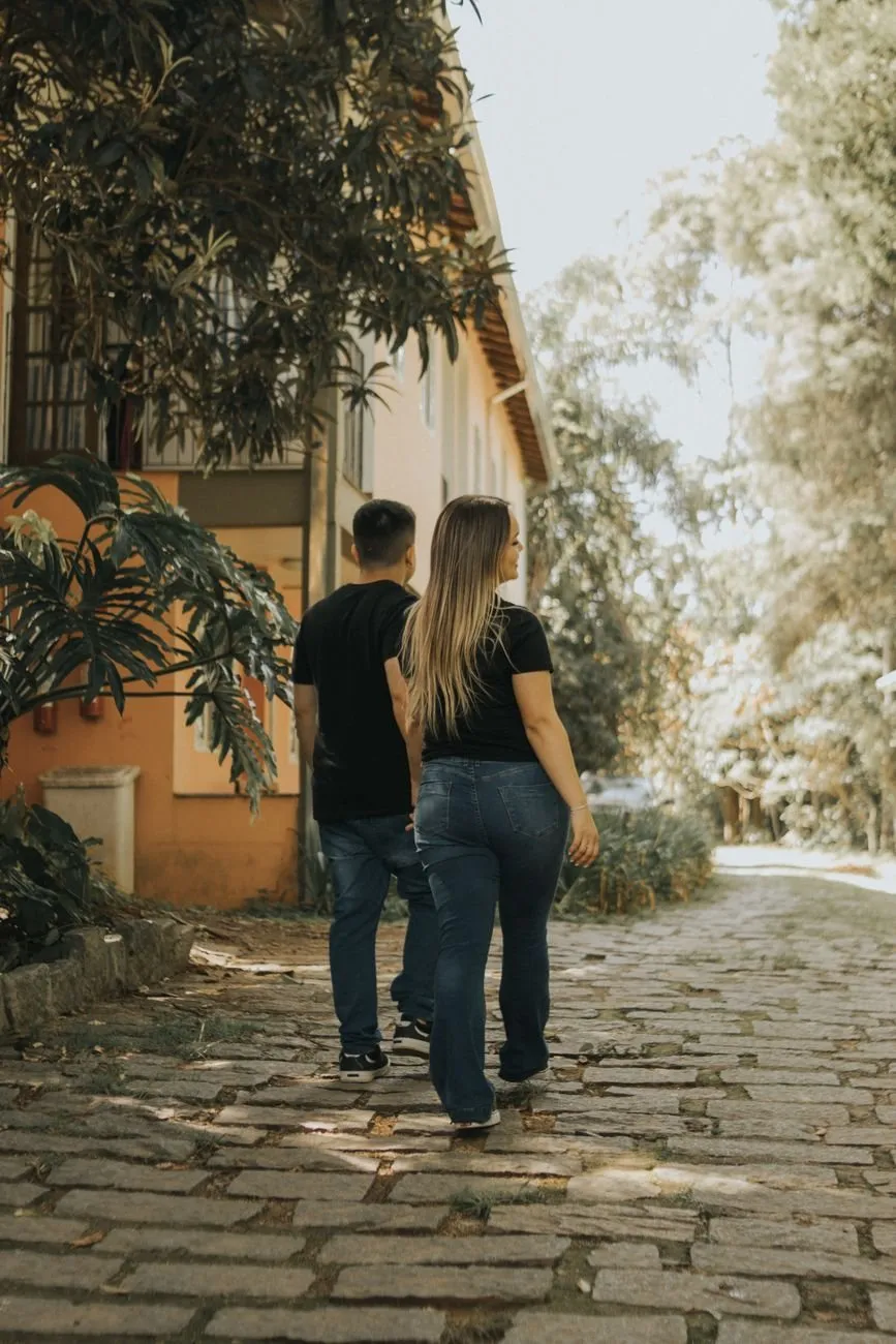 A couple seen from behind, walking up a sunlit cobbled lane towards a house