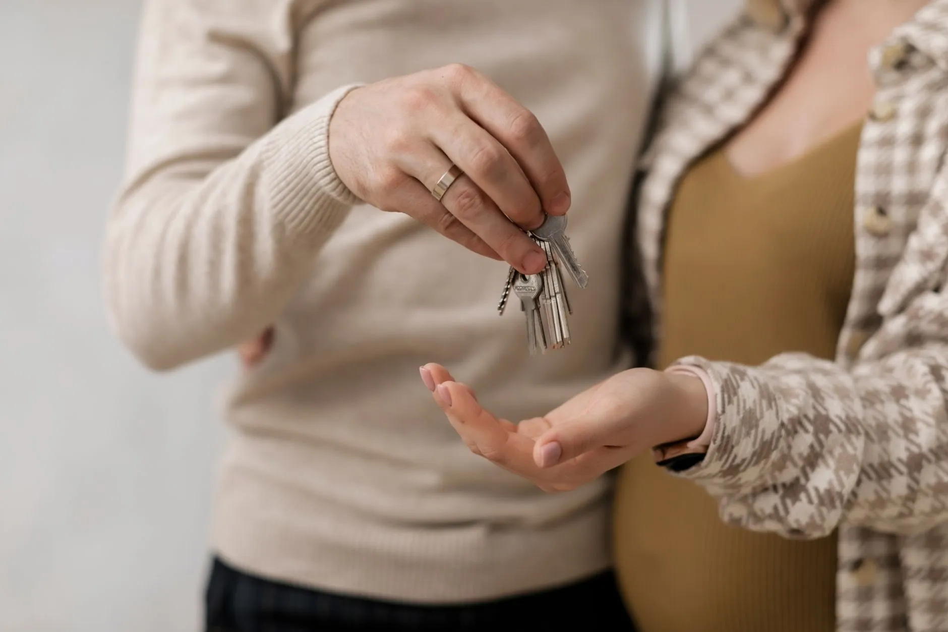 A couple's hands, one dropping a set of house keys into the other's open palm