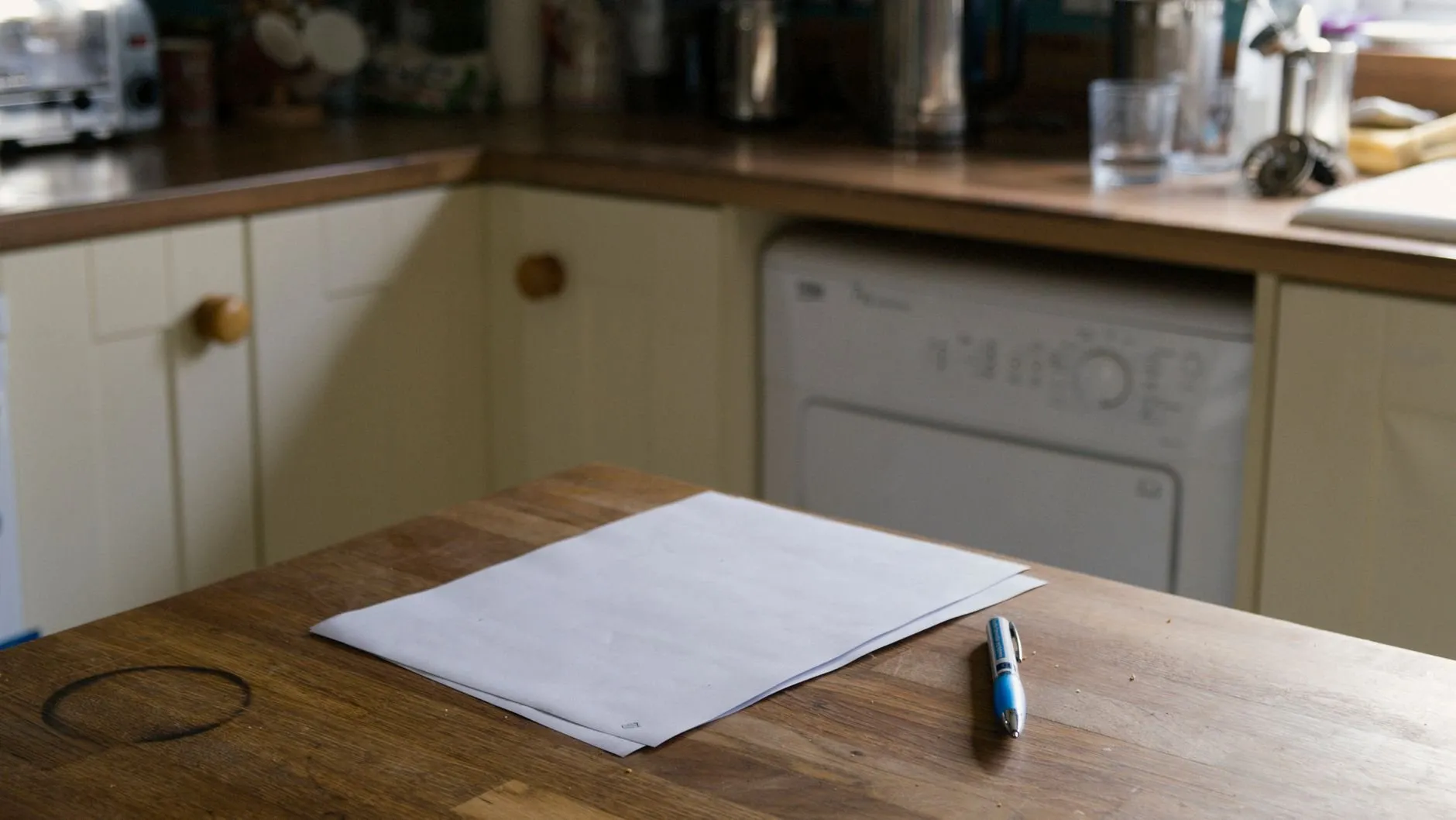 A sheet of paper and a pen on a worn wooden kitchen table