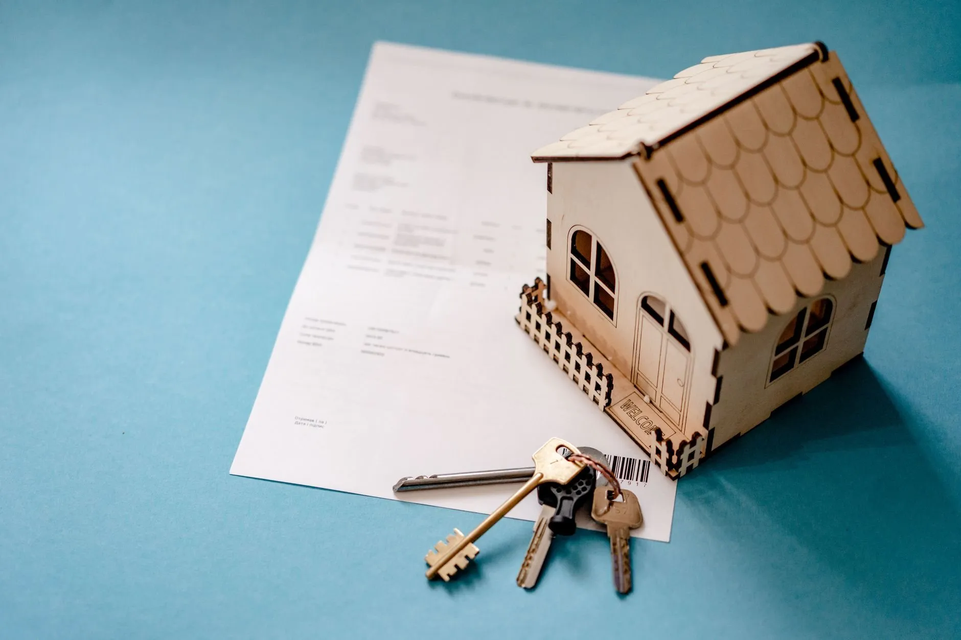 A small plywood model house on a signed document with a bunch of keys beside it