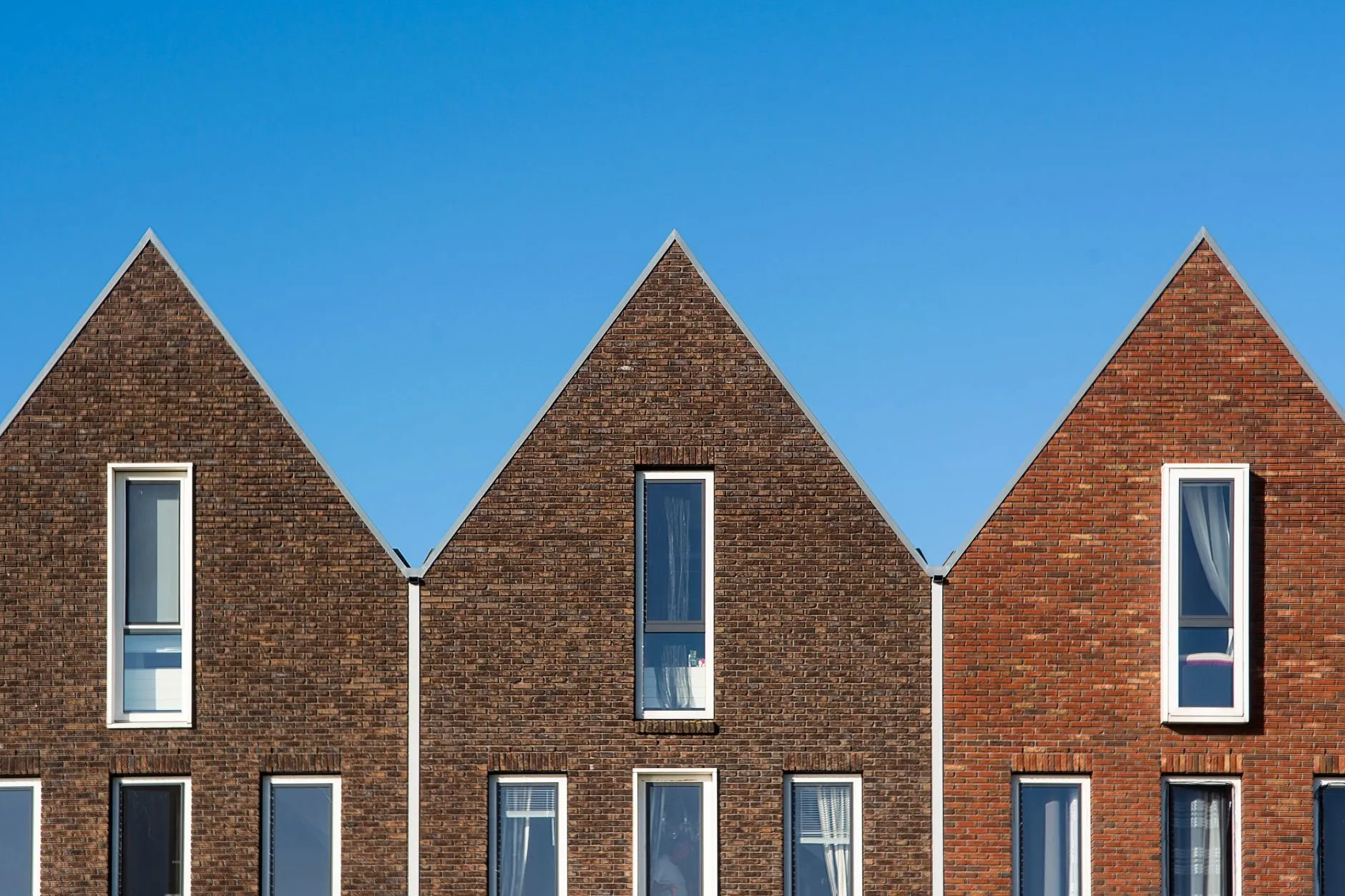 Three new-build brick houses with steep gables under a clear blue sky