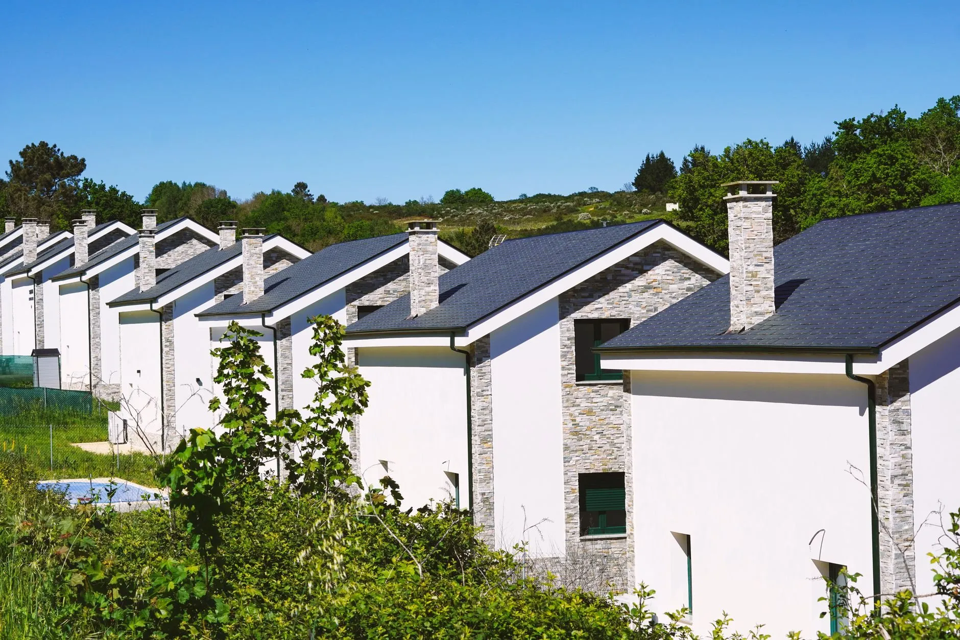 A row of white new-build houses with slate roofs and stone chimneys among green trees
