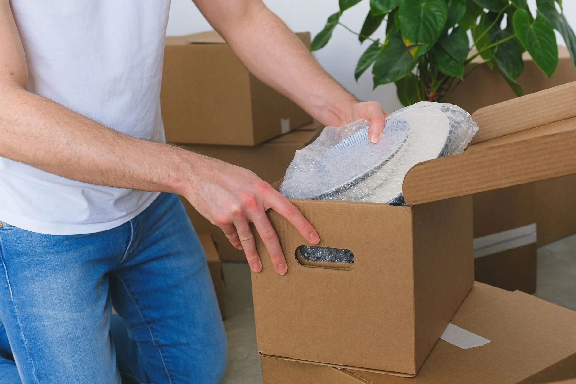 Hands wrapping plates in bubble wrap and packing them into a cardboard box