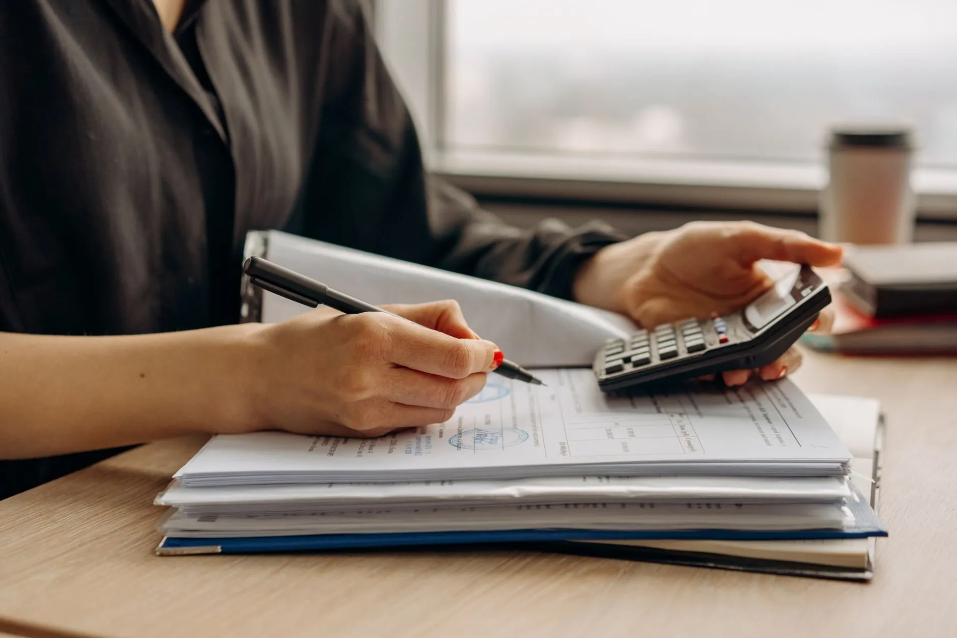 Hands working through a stack of accounts with a pen and a calculator